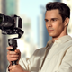 A user holding the DJI RS 3 Mini stabilizer's handle with two hands while staring at the preview screen on the camera.